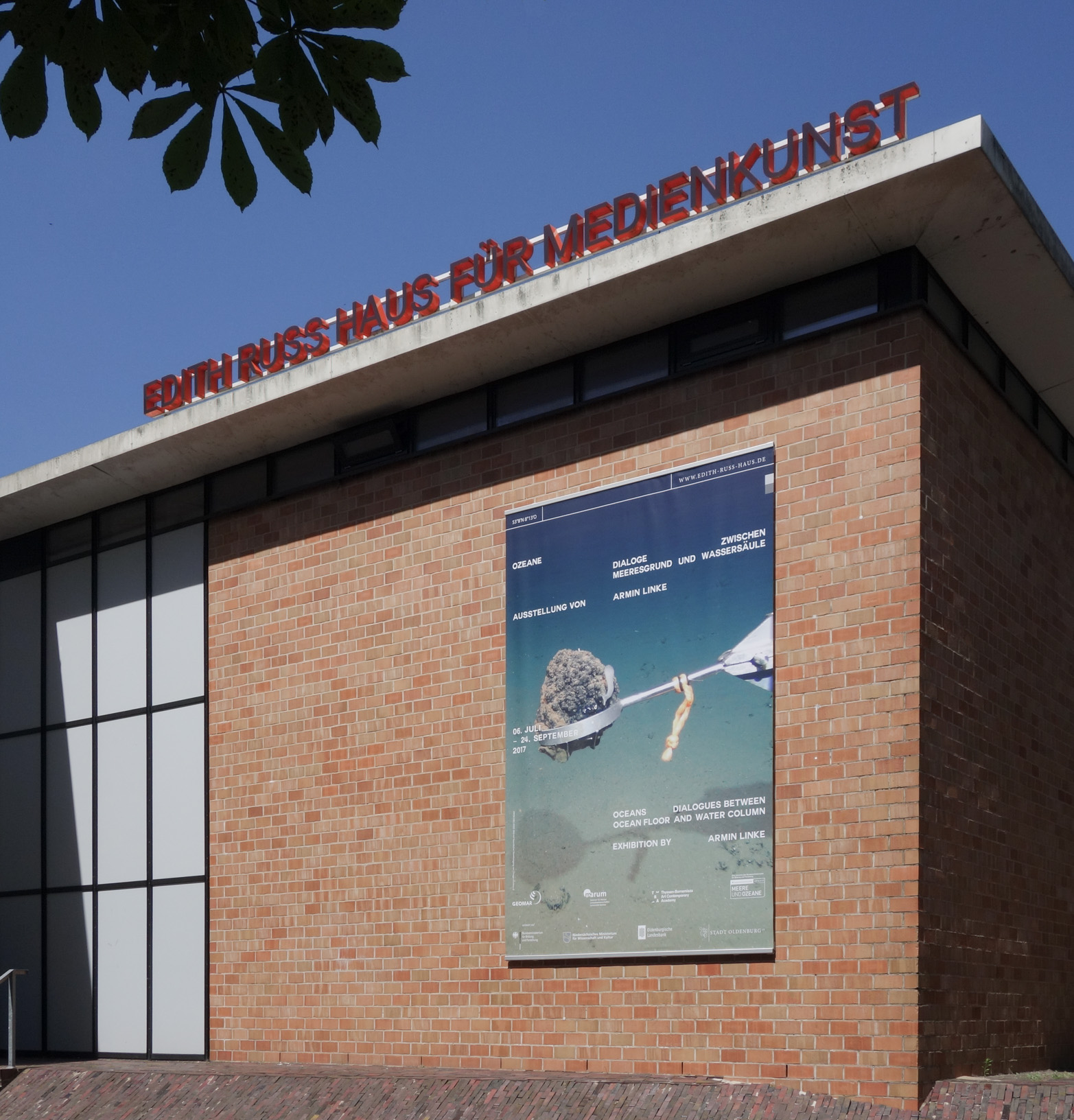 Das Foto zeigt die Fassade des Edith-Russ-Hauses mit dem Banner zur Ausstellung Armin Linke: Ozeane – Dialoge zwischen Meeresgrund und Wassersäule. Foto © Edith-Russ-Haus